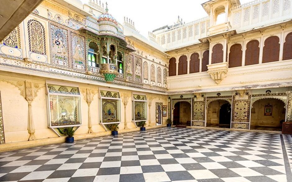 A grand courtyard at the City Palace Museum, Udaipur. There is a checkerboard floor and ornate architecture.