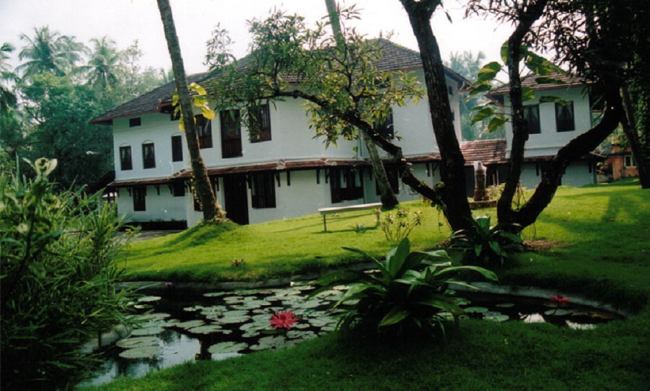 Harivihar Retreat - a white building in the background with trees and a stream in the front