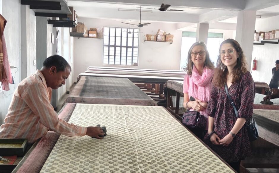 Photo of Jocelyn and companion smiling while block printer prints on fabric