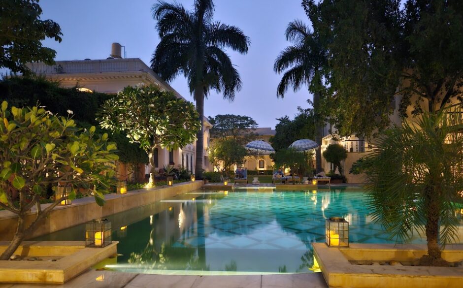 Photo of Royal Heritage Haveli in Jaipur, a large hotel pool at night with palm trees in the background